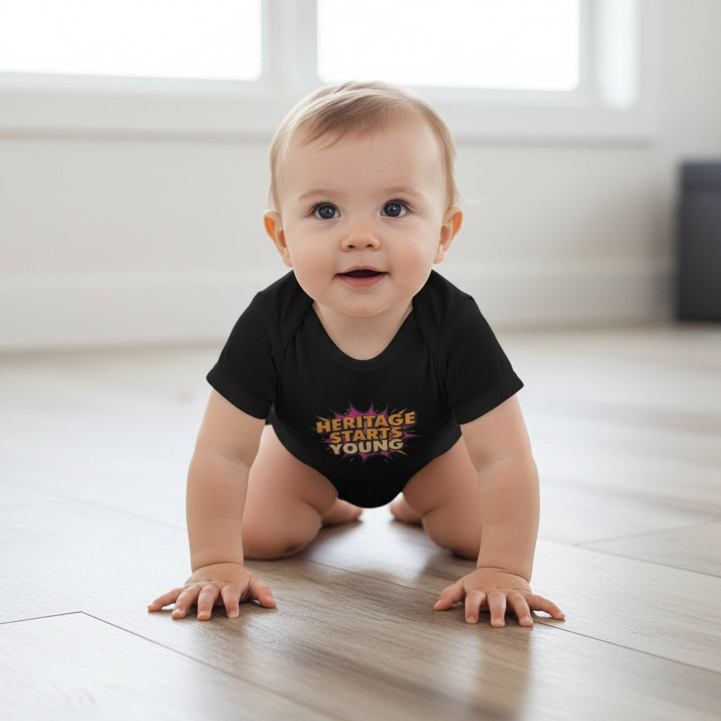 Baby crawling on a wooden floor wearing a black onesie with text.(heritage starts young)